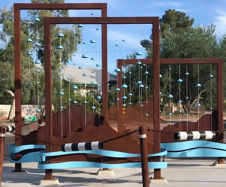 Rust-colored steel frames with hanging blue ceramic pieces at a Third Street intersection