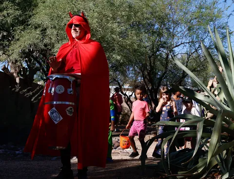 A neighbor in a red devil costume hands out candy to children at the Pocket Park